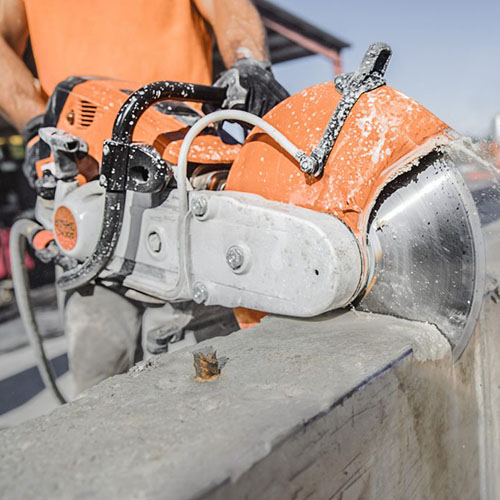Worker in orange cutting through concrete with a cut-off saw